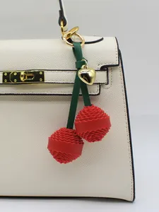 Macro detail of a 3D red textured cherry bag charm featuring a gold heart pendant charm
