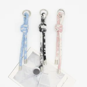 Dettaglio di tre ciondoli per borsa in denim intrecciato con paillettes in blu, nero e rosa.