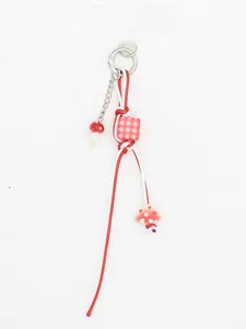 Gros plan d'un bijou de téléphone tressé rouge et blanc avec champignon et perle à carreaux