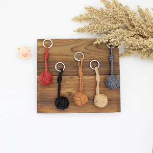 Detail of five hand-woven PU leather ball keychains in various colors on wooden display stand