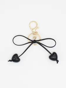 Detailed shot of minimalist black bow keychain with heart charms and gold clasp