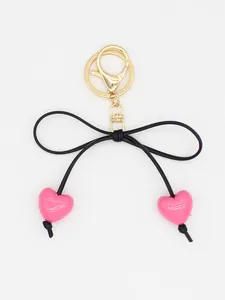 Detailed close-up of cute macaron pink heart beads and black bow on a gold keychain clasp