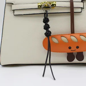 Close-up of handmade orange bread leather charm accessory hanging on a white bag