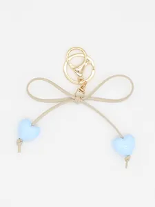 Detail view of a cute macaron heart bow keychain charm with gold clasp on white background.
