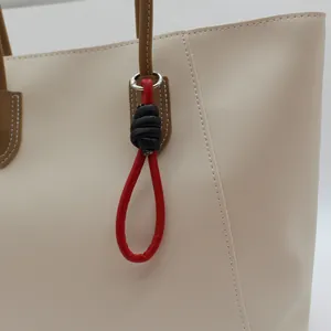 Close-up detail of a red and black PU leather braided loop charm on a beige tote bag