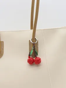 Handmade red woven cherry bag charm with green leaves attached to a cream tote bag.