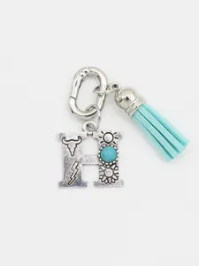 Detail of silver letter H bag charm with turquoise stone and aqua blue tassel