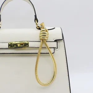 Close-up of gold PU leather woven wrist strap keychain attached to a white handbag