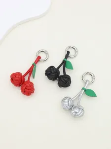 Close-up of handmade woven PU leather cherry bag charms in red, black, and silver.