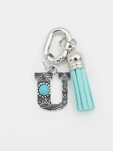 Detailed view of ethnic style metal letter U bag charm with blue tassel and turquoise