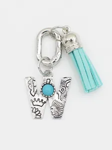 Detailed view of an ethnic silver letter W charm with turquoise and blue tassel