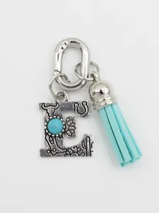 Detailed macro view of ethnic style silver letter E charm with turquoise stone and blue tassel
