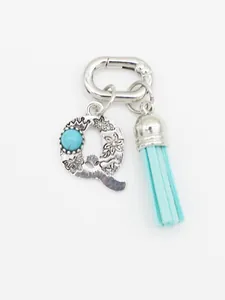 Close-up of silver engraved letter Q charm with turquoise bead and blue tassel.