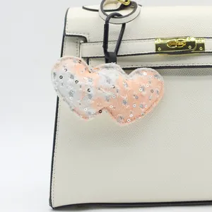 Close-up of denim plaid heart keychain with silver sequins on a white leather bag.