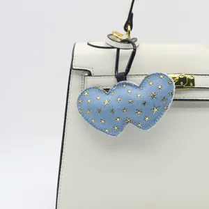Detail showing denim double heart bag charm with gold stars hanging on white bag