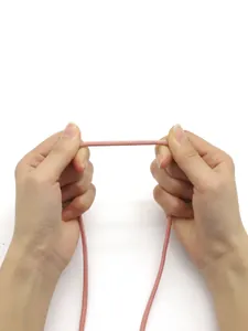 Close-up of hands pulling a matte pink stitched round leather cord for DIY craft projects