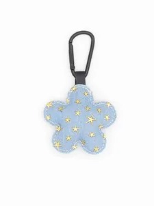 Primer plano de un llavero de flor vaquera azul con lentejuelas de estrellas doradas y clip negro.