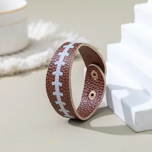 Detail view of brown PU leather bracelet with white football stitching and snap buttons.