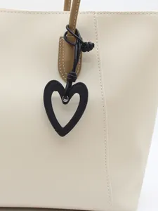 Nahaufnahme eines minimalistischen schwarzen hohlen Herzanhängers an einer cremefarbenen Tasche