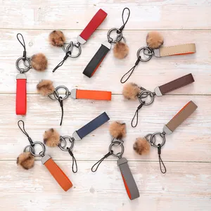 Bunte Leder-Schlüsselanhänger mit weichen Pelzkugeln auf heller Holzoberfläche