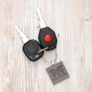 Close-up of vintage silver square keychain with an engraved floral letter M detail.