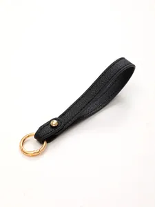 Close-up of black pebbled leather strap keychain with gold metal ring detail