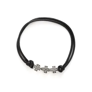 Close-up view of black woven waxed cord bracelet featuring three silver cross charms on white.