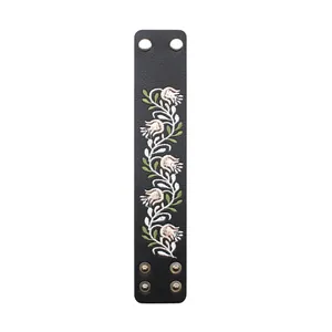 Detailed macro view of folk style black PU leather cuff with white floral embroidery.