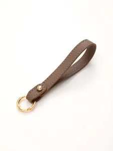 Close-up detail of a brown pebbled leather wrist strap keychain with a gold metal ring