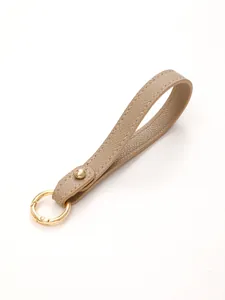 Detailed view of a beige pebble leather keychain strap with a gold-tone spring ring.