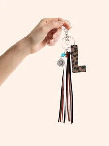 Close-up of a leopard print leather letter L keychain with long tassels held by a hand
