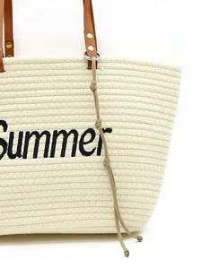 Close-up of a handmade woven rope bag pendant attached to a summer straw tote bag