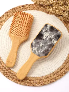 Macro detail showing cow print leather texture on a bamboo paddle hairbrush on a woven mat
