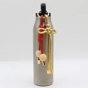 Detalle de un adorno de cuero PU trenzado con nudo chino colgado de una botella de agua.