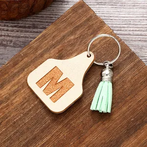 Detail view of a farm-style keychain featuring an engraved letter M and mint green tassel.