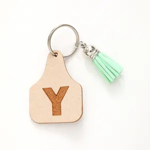Close-up of leather ear tag keychain with engraved letter Y and mint green tassel