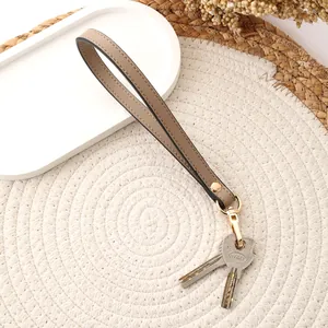 Taupe leather wristlet strap with gold clasp holding keys on a woven mat.