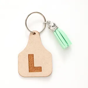 Detailed view of a minimalist beige ear tag keychain with letter L and mint green tassel