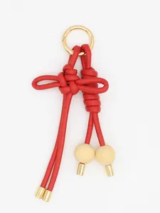 Detalle de un llavero de cuero PU trenzado rojo con nudo y cuentas de madera fina.
