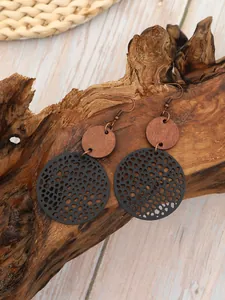 Dettaglio di orecchini pendenti circolari in legno e rete nera su legno naturale.