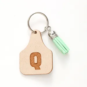 Detail of faux leather cow tag keychain featuring letter Q and soft green tassel