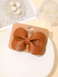 Detailweergave van een bruine leren strik haarklem op een presentatiekaart.