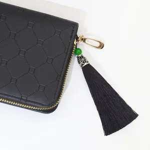 Detail of black polyester tassel charm with green bead on a black wallet zipper
