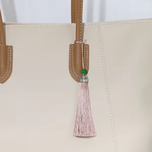 Close-up detail of pink silky tassel with green bead and silver cap on a beige tote bag
