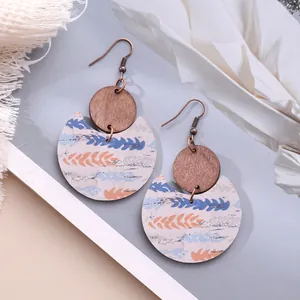 Detailed macro view of crescent earrings featuring wood disks and colorful feather patterns