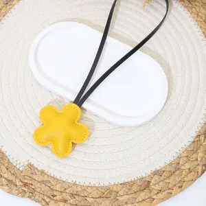 Close-up detail of a cute yellow leather flower bag charm with black cord on a woven mat
