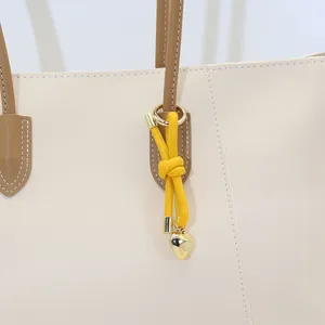 Close-up view of a minimalist yellow leather knot bag charm with gold heart pendant