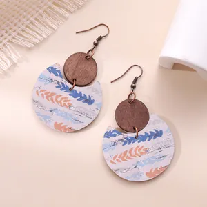 Detail of crescent-shaped earrings combining natural wood and patterned leather textures.