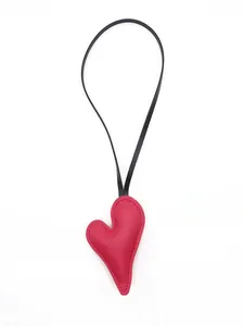 Detail macro view of a red pebbled leather heart-shaped bag charm with black strap