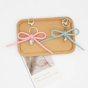 Woven leather bow keychains in pink and grey with silver heart charms on wooden tray